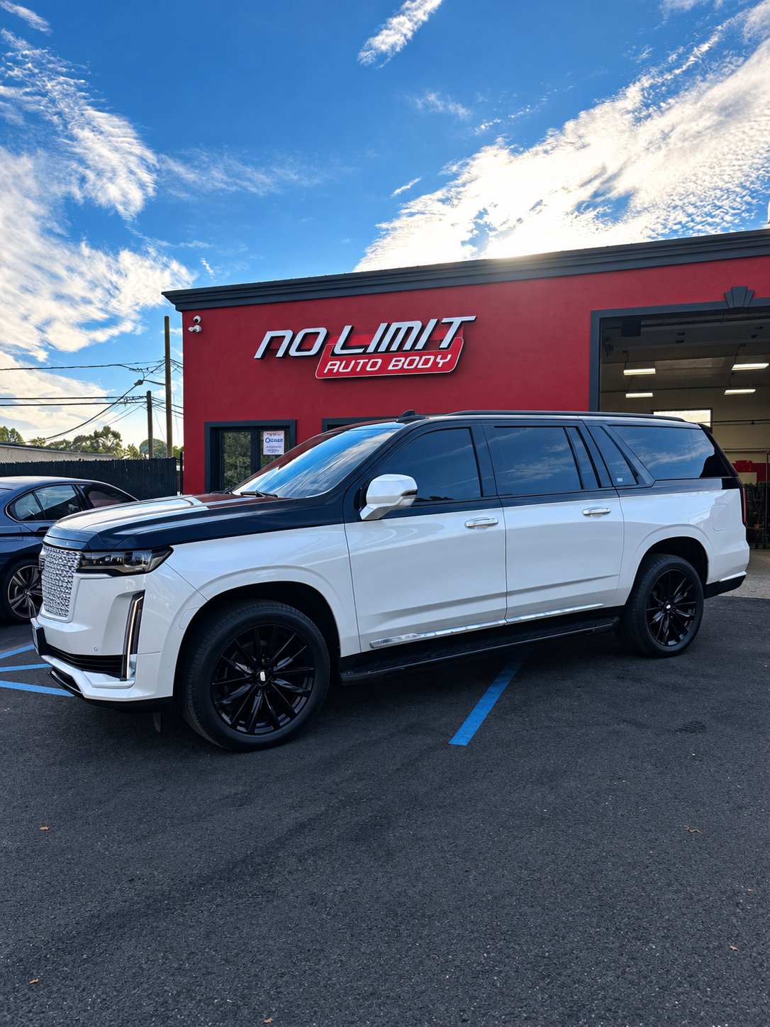White Cadillac Escalade parked in front of the red No Limit Auto Body building