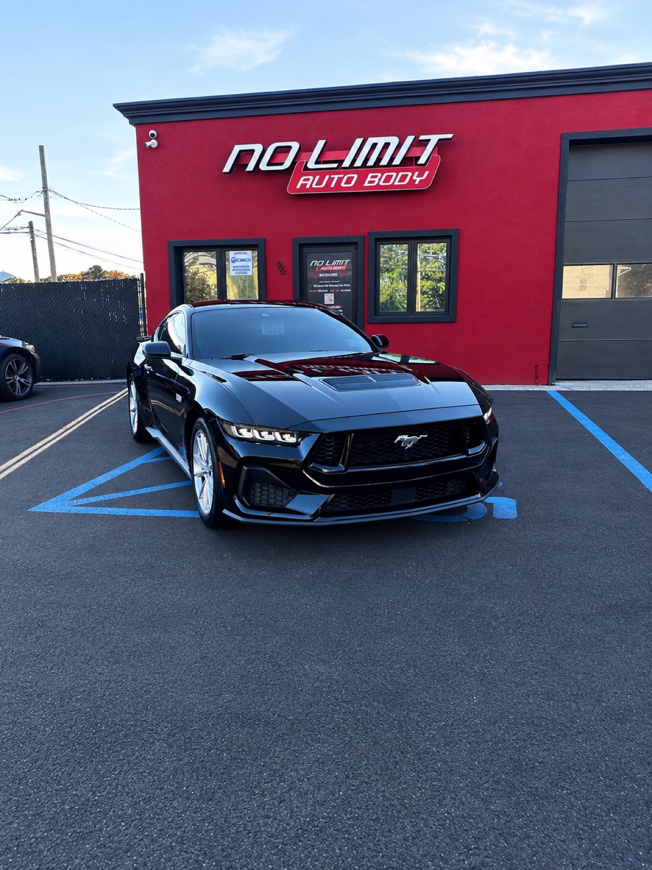 Black Ford Mustang S650 in front of the red No Limit Auto Body building
